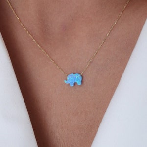 May include: A delicate gold chain necklace with a blue opal elephant pendant.