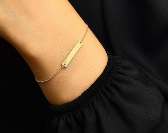 Op de afbeelding: Een gouden armband met een staaf en een delicate ketting. De armband wordt om de pols gedragen.