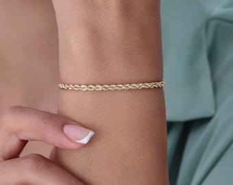 Könnte beinhalten: Ein goldenes Seilkettenarmband am Handgelenk einer Person.