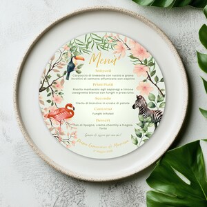 Può includere: Un menu circolare con un design floreale, con un tucano, un fenicottero e una zebra. Il menu include testo italiano per antipasti, primi piatti, secondo, contorno e dessert. La carta è su un piatto bianco.