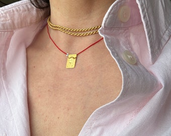 May include: A person wearing a pink button-down shirt with a gold chain necklace and a red string necklace with a small gold pendant.
