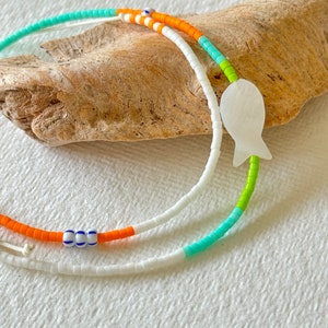 May include: A white beaded necklace with orange, turquoise, and green beads. The necklace features a white shell fish charm.