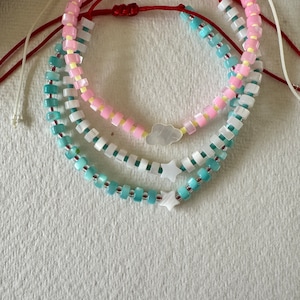 Peut inclure: Trois bracelets superposés avec des perles roses, blanches et bleues. Les bracelets présentent un charme nuage blanc et deux charmes étoiles blancs.