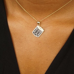 May include: A gold chain necklace with a small gold drum pendant.