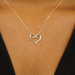May include: A gold necklace with a heart-shaped pendant featuring an infinity symbol. The pendant is adorned with small, clear stones.