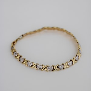 Puede incluir: Pulsera dorada con un patr&oacute;n repetido de corazones y X. La pulsera tiene un dise&ntilde;o de cadena delicado y probablemente est&aacute; hecha de oro o metal chapado en oro. Los corazones tienen una apariencia texturizada.