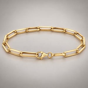 May include: A 14K yellow gold paperclip chain bracelet featuring elongated rectangular links connected in a continuous loop. The bracelet is secured with a lobster claw clasp that is clearly stamped with the text 14K.