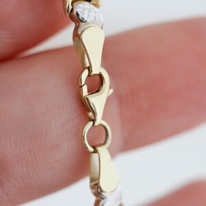 Puede incluir: Una pulsera dorada y plateada con un dise&ntilde;o de X y O. La pulsera tiene un cierre de mosquet&oacute;n. La pulsera est&aacute; hecha de metal dorado y plateado. La pulsera es una joya.