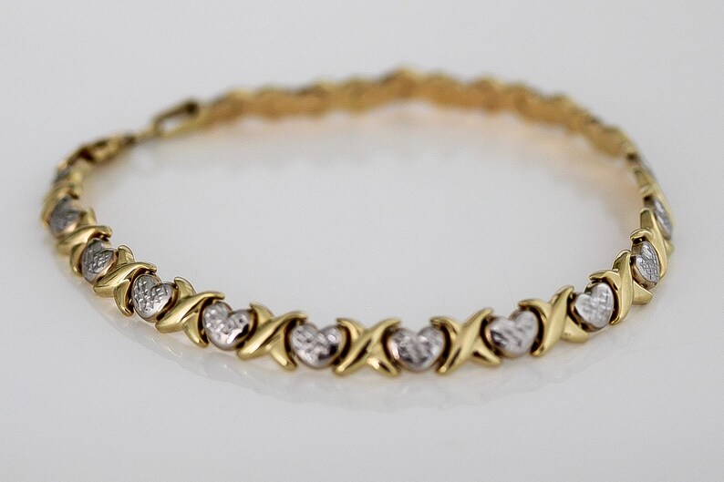 Puede incluir: Pulsera dorada con eslabones alternos en forma de X y coraz&oacute;n. Los corazones tienen un acabado texturizado de color plateado. Una joya delicada, adecuada para el uso diario o ocasiones especiales.