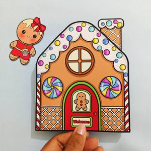 Puede incluir: Una colorida casa de jengibre y un recorte de hombre de jengibre. La casa presenta una puerta roja con un hombre de jengibre, una ventana redonda y acentos de caramelos coloridos. La palabra "Welcome" está en la puerta. El hombre de jengibre tiene un lazo rojo.