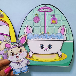 Może przedstawiać: Różowa i biała wanna dla króliczka z prysznicem i butelką mydła. Wanna jest otoczona zielonym i białym kafelkowym tłem. Różowy króliczek z opaską na głowie stoi przed wanną.