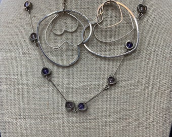 Silver tone heart necklace with clear and purple beads. Lobster clasp. 16 inches long. 1 pair of pierced heart dangle earrings.