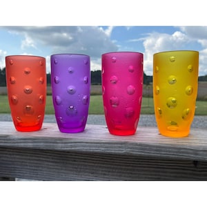 Puede incluir: Cuatro vasos de beber coloridos con una superficie texturizada y con burbujas. Los vasos son naranja, morado, rosa y amarillo.