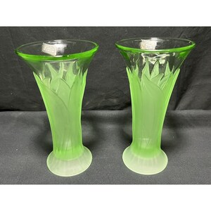 Puede incluir: Dos jarrones de vidrio verde con acabado esmerilado y dise&ntilde;o de hojas. Los jarrones miden aproximadamente 20 cm de alto.