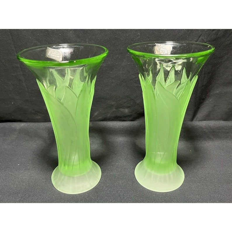 Puede incluir: Dos jarrones de vidrio verde con acabado esmerilado y dise&ntilde;o de hojas. Los jarrones miden aproximadamente 20 cm de alto.