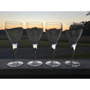 May include: Four clear glass wine glasses with a sunset reflected in them. The glasses are arranged in a row on a wooden surface.