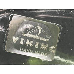 Puede incluir: Una etiqueta de vidrio transparente con el texto "VIKING HAND MADE" y una imagen estilizada de un barco vikingo.