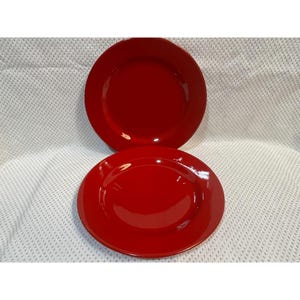 May include: Two glossy, red ceramic plates. The plates are round with a slightly raised edge. The plates are a solid, vibrant red color and appear to be new. The plates are likely for serving food.