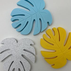 May include: Three tropical leaf-shaped coasters in different colors: light blue, white with a speckled texture, and yellow.