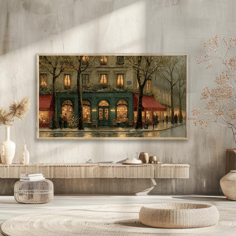 Pode incluir: Uma impress&atilde;o emoldurada retrata uma cena de rua parisiense de inverno. O edif&iacute;cio turquesa com toldos vermelhos &eacute; iluminado por luzes internas quentes. &Aacute;rvores nuas ladeiam a rua e figuras caminham pela cal&ccedil;ada. A obra de arte &eacute; exibida acima de uma consola tecida.