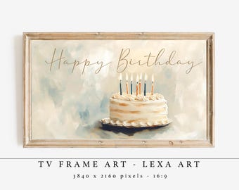 May include: A framed art print featuring a birthday cake with lit candles. The words "Happy Birthday" are written in elegant script above the cake. The artwork has a soft, watercolor-like background in shades of blue and white.