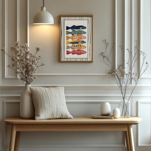 May include: A framed art print displaying six vibrant fish illustrations. The fish are in various colours and patterns, including blue, green, yellow, and red. The artwork is set against a cream background with a brown frame and black and white striped accents.