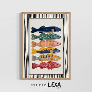 May include: A framed art print showcasing six illustrated fish in vibrant colours. The fish are arranged vertically on a cream background, each with distinct patterns and shades of blue, yellow, orange, and pink. The frame is light wood with a black and white striped border.