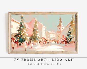 Op de afbeelding: Een ingelijste digitale kunstprint met een kerstmarkt in een winters tafereel. Het kunstwerk toont gebouwen met roze daken, besneeuwde straten en versierde kerstbomen. De tekst "TV FRAME ART - LEXA ART" staat onderaan.