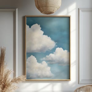 Peut inclure: Une impression d'art encadrée représentant un ciel serein avec des nuages blancs duveteux sur un fond bleu clair. L'œuvre est encadrée dans un cadre en bois brun clair, créant une esthétique apaisante. L'impression est affichée sur un mur blanc.