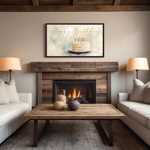 May include: A framed art print featuring a birthday cake with lit candles. The words "Happy Birthday" are written in elegant script above the cake. The artwork hangs above a fireplace in a cozy living room setting.