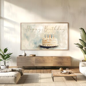 May include: A framed art print featuring a watercolor painting of a birthday cake with lit candles. The words "Happy Birthday" are written in gold script above the cake. The background is a soft blend of blue and white.