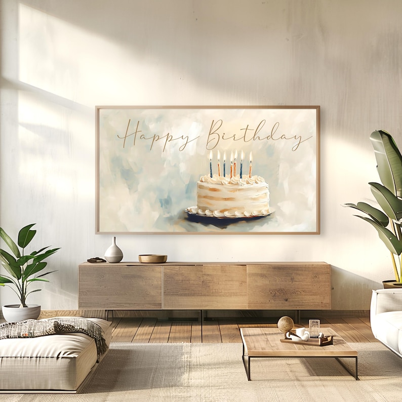 May include: A framed art print featuring a watercolor painting of a birthday cake with lit candles. The words "Happy Birthday" are written in gold script above the cake. The background is a soft blend of blue and white.