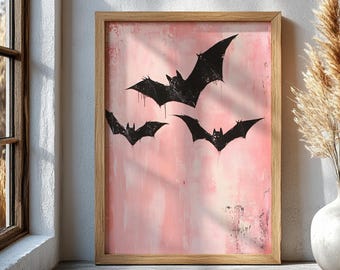 May include: A framed art print featuring three black bat silhouettes against a pink and white textured background. The bats have a dripping paint effect. The frame is made of light brown wood. The artwork is displayed near a window.