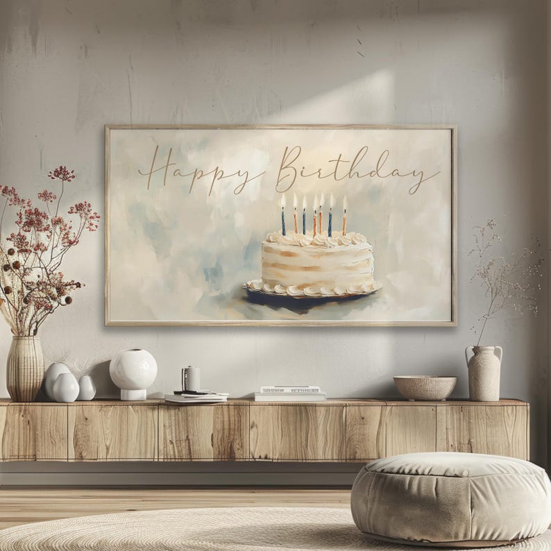 May include: A framed print featuring a watercolor painting of a birthday cake with lit candles. The words "Happy Birthday" are written in elegant script above the cake. The artwork has a soft, pastel color palette and is displayed on a wooden console.