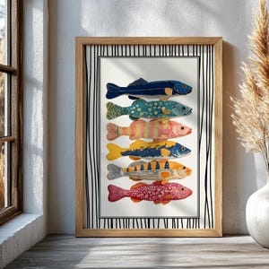 May include: A framed art print showcasing six vibrantly coloured fish illustrations. Each fish displays a unique pattern in shades of blue, yellow, orange, and pink. The artwork is set against a white background with a black and white striped border, within a wooden frame.