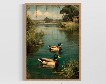 Op de afbeelding: Een ingelijste vintage kunstdruk toont twee wilde eenden die in een rustige vijver zwemmen. De eenden hebben groene koppen, bruine lichamen en gele snavels. Het kunstwerk toont een sereen landschap met weelderig groen, een klein gebouw en een bewolkte lucht.