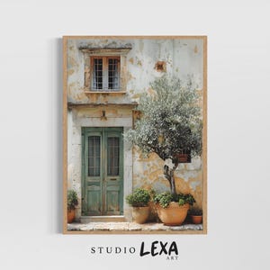 May include: A framed print depicting a European building with a green door and window. An olive tree and potted plants are outside. The building has a weathered facade. The print is labeled "STUDIO LEXA ART".