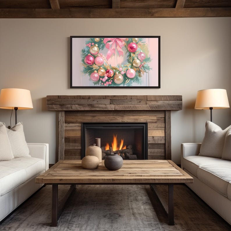 Op de afbeelding: Een ingelijst kunstwerk met een kerstkrans met roze en gouden ornamenten en een roze strik. Het kunstwerk hangt boven een open haard met een brandend vuur. De kamer heeft een rustieke houten salontafel, twee lampen en twee witte banken.