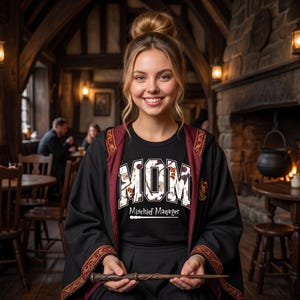 May include: A black t-shirt featuring the word MOM in large block letters filled with a pattern of magical icons, with the text Mischief Manager and a wand graphic underneath. The shirt is worn under a black robe with a dark red lining and gold trim.
