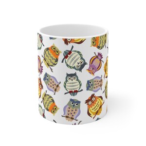 May include: White ceramic mug featuring a repeating pattern of colorful cartoon owls. The owls are depicted in various poses and colors, including orange, blue, yellow, and purple. The mug is a standard size and shape.