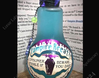 May include: A blue glass bottle with a purple and white label that reads "Vampire Breath". The label has a warning that says "Beware... You Dare" and instructions to "Consumer Inhale If Open Wide and Say... Mouthwash".
