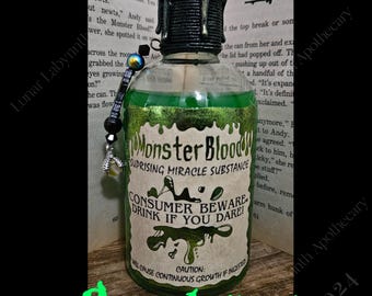 May include: A small glass bottle containing a green liquid. The bottle has a black and white label that reads "Monster Blood" and "Surprising Miracle Substance". The label also features a warning that says "Consumer Beware! Drink if you Dare!" The bottle has a black and silver metal cap with a green wax seal. The bottle is resting on a wooden surface with a book in the background. The book has the title "Goosebumps" on the cover.