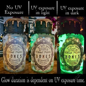 Op de afbeelding: Drie glazen flessen met zwarte en gouden etiketten waarop "Dead Men's Bones" staat, die onder UV-licht groen oplichten. De flessen staan op een donkere achtergrond.
