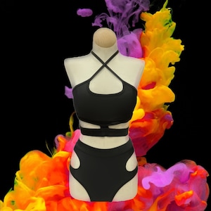 Könnte beinhalten: Schwarzes zweiteiliges Tanzoutfit mit einem Halfter-Oberteil und einer hoch sitzenden Hose. Das Oberteil hat ein Kreuzdesign und einen Ausschnitt vorne. Die Hose hat einen hohen Bund und einen Ausschnitt an jeder Seite.