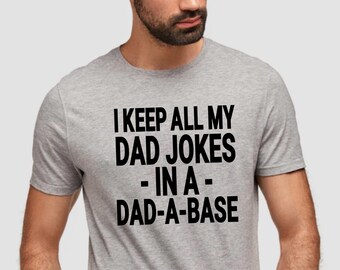 May include: A gray t-shirt with the text "I keep all my dad jokes - in a - dad-a-base" printed in black.