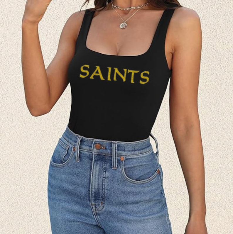 May include: A black tank top with a gold "SAINTS" graphic. The tank top is worn by a person with blue jeans.
