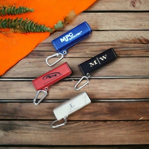 Può includere: Quattro portachiavi con diversi foderi in pelle colorati e anelli metallici. I foderi sono blu, nero, rosso e bianco. Il fodero blu ha il testo "MPC" e "Mechanical Pipe Contractors". Il fodero nero ha il testo "M|W". Il fodero rosso ha il testo "Allstate Contracting Inc.". Il fodero bianco ha il testo "Lila Grace".