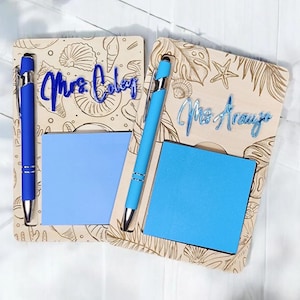 May include: Two wooden memo boards with blue pens and sticky notes. One board has the name "Mrs. Coley" in blue script, and the other has "Mrs. Arayo". The boards are decorated with etched seashell and tropical leaf designs.