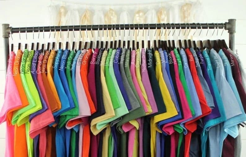 K&ouml;nnte beinhalten: Ein Gestell mit T-Shirts in verschiedenen Farben, darunter Neonorange, Neongr&uuml;n, Neongelb, S&auml;urelila, Korallen Seide, Texas Orange, Saphir, Neonblau, Irisch Gr&uuml;n, Orange, Beere, Brombeere, Kobalt, Azalee, Seidenmais, Heide-Orchidee, Mitternachtsblau, G&auml;nsebl&uuml;mchen, Violett, K&ouml;nigsblau, Schwarz, Heliconia, Rasen Gr&uuml;n, Carolina Blau, Rot, Indigo Blau, Lila, Tropisches Blau, Hellblau, Himmelblau, Maroon und Sport Grau.