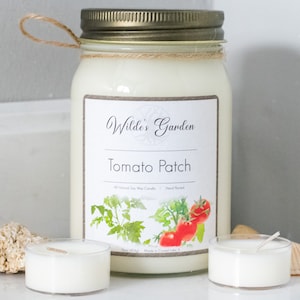 May include: A glass jar candle with a gold lid and a white label that reads "Wilde's Garden Tomato Patch All Natural Soy Wax Candle Hand Poured". The label features a watercolor illustration of tomato plants and ripe red tomatoes.